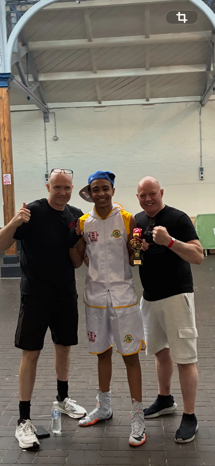 A young champion holding his trophy with two Cricklewood coaches